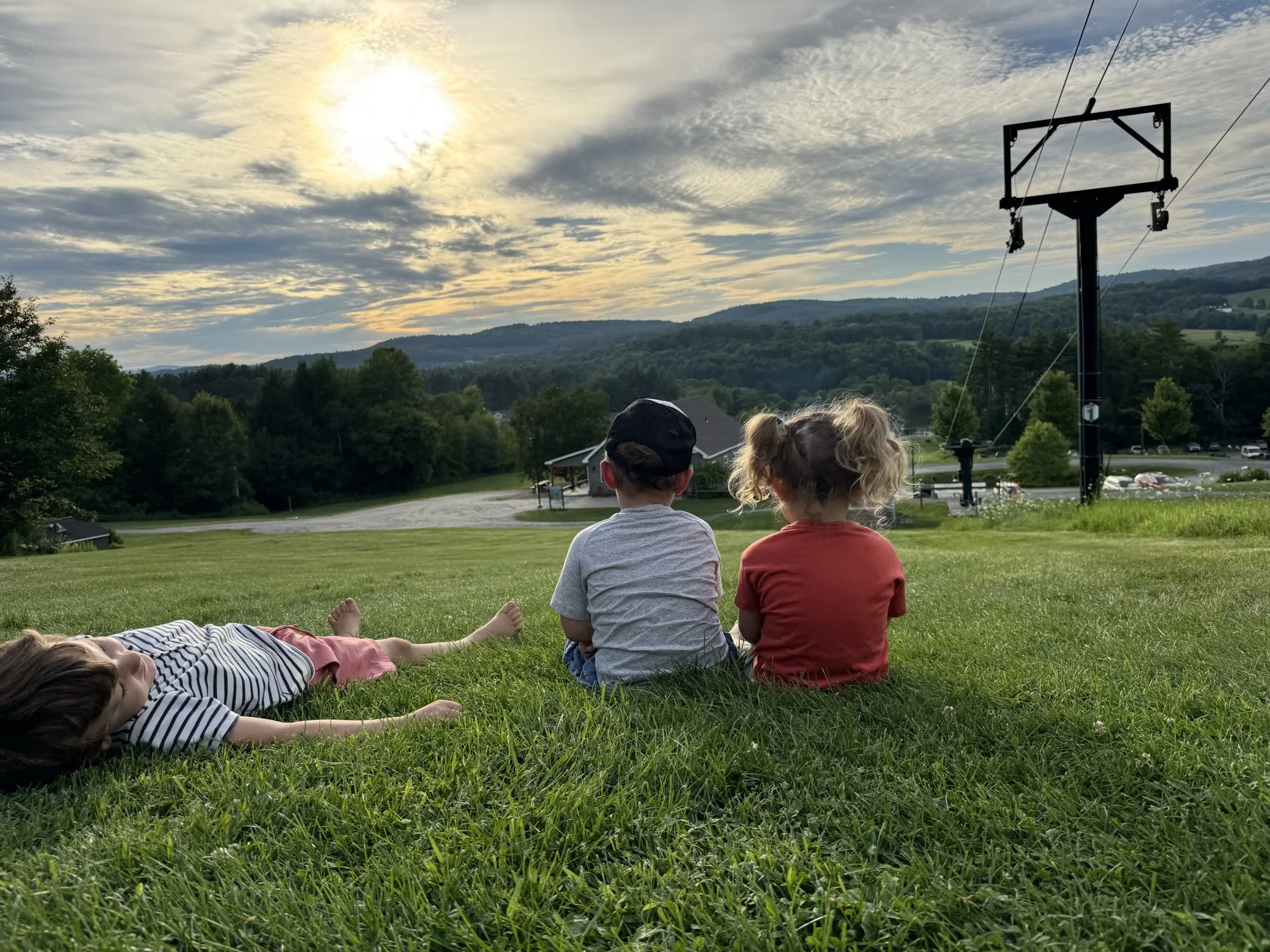 Children relaxing on a grassy hillside at sunset with mountains beyond